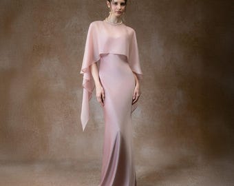 May include: A floor-length, blush pink gown with a matching sheer cape. The dress has a fitted silhouette that flares out slightly at the bottom. The cape drapes over the shoulders and arms, creating a flowing effect. The overall look is elegant and formal.