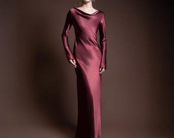 May include: A long, burgundy-colored satin dress with long sleeves and a cowl neckline. The dress is floor-length and has a sleek, elegant silhouette. The model is wearing sunglasses and gold earrings.