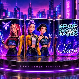 Puede incluir: Una taza de cerámica blanca con asa en forma de corazón que presenta un gráfico vibrante de tres personajes estilo anime en una ciudad de neón. El diseño incluye el texto K-POP DEMON HUNTERS y el nombre Clara en fuente cursiva sobre fondo morado.