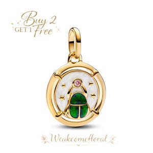 May include: Gold-toned pendant with a circular design featuring a green and blue scarab beetle, a pink gem, and white enamel. The pendant has a gold bail for attaching to a chain. The text "Buy 2 Get 1 Free" is in the upper left corner.