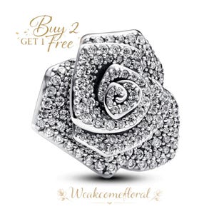 May include: A silver rose-shaped charm, covered in numerous clear, sparkling crystals. The charm has a detailed, layered design, with the text "Buy 2 Get 1 Free" in gold script. The shop's name, "Weakcomefloral", is also displayed.