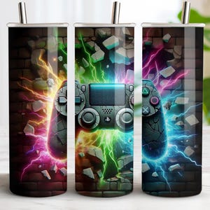 May include: Three stainless steel insulated tumblers with a gaming theme. Each tumbler features a cracked brick wall design with a video game controller and colorful lightning effects in shades of pink, green, and blue.