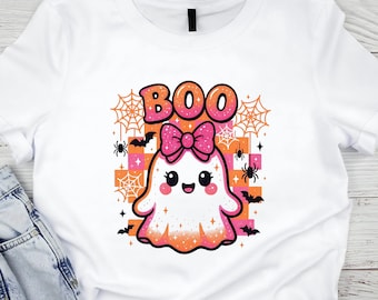 May include: White t-shirt with a cartoon ghost design. The ghost has a pink bow and the word "BOO" in orange and pink above it. The design includes bats, spiders, and spiderwebs, set against a checkered orange and pink background. A Halloween-themed graphic.