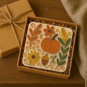 Pode incluir: Um papel creme com desenhos de outono em quilling, incluindo uma abóbora, flores, folhas e uma bolota. A obra de arte é apresentada numa caixa de presente castanha com papel picado e uma caixa separada embrulhada com fio.