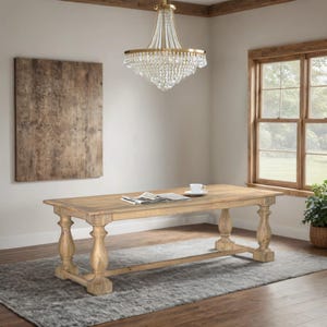 May include: A light-colored wooden dining table with turned legs, a rectangular top, and a lower stretcher. A newspaper and a teacup sit on the table. A crystal chandelier hangs above the table. The table is on a gray rug.