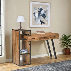 May include: A wooden desk with three drawers and black metal legs. The desk has a built-in side shelf unit with open shelving. A white lamp sits on top of the shelf unit. A framed abstract painting hangs above the desk.