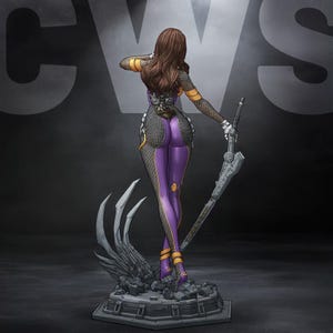 Pode incluir: Uma figura colecionável de uma personagem com longos cabelos castanhos, vestindo um traje texturizado roxo e preto com detalhes amarelos. A figura está sobre uma base rochosa escura e segura uma longa espada metálica em uma das mãos.