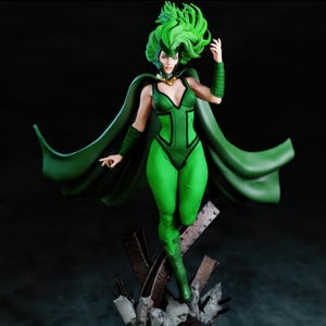 May include: A green figurine of a female character with green hair and a matching costume. The figure is posed dynamically, with a flowing cape and a determined expression. The base appears to be made of metal and concrete.