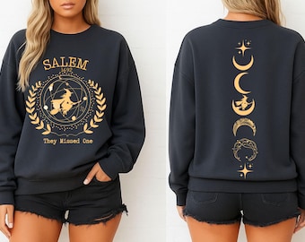 May include: Dark gray sweatshirt with gold Salem 1692 witch graphic on the front and moon phase design on the back. The front graphic includes a witch on a broom inside a circle with text "They Missed One".