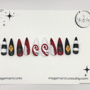 May include: A set of ten false nails with a variety of designs. The nails feature black, white, and red colors with patterns including stripes, crosses, and abstract shapes. The text "@magemanicures" and "magemanicures.etsy.com" are visible.