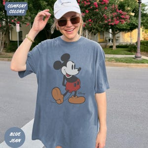 May include: Blue jean coloured t-shirt featuring a classic Mickey Mouse graphic. The cartoon character is depicted in black, white, red, and tan. The shirt has the words "Comfort Colors" and "Blue Jean" in the corners.