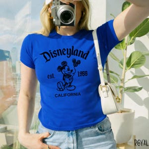 May include: Royal blue t-shirt with a black Disneyland graphic featuring Mickey Mouse, the text "est. 1955", and "CALIFORNIA". The shirt has short sleeves and a crew neck.