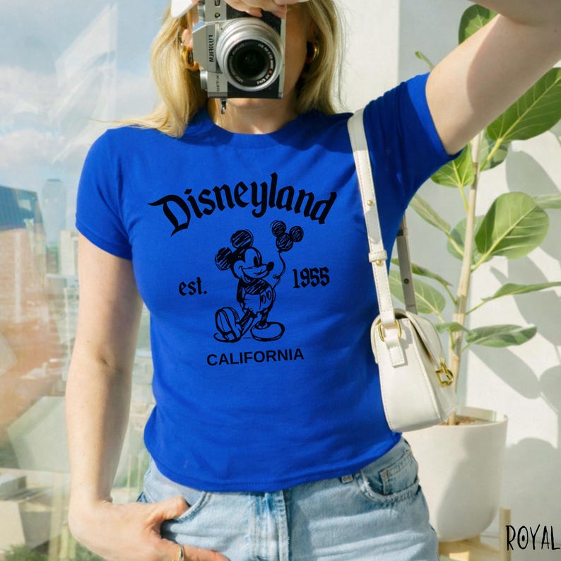 May include: Royal blue t-shirt with a black Disneyland graphic featuring Mickey Mouse, the text "est. 1955", and "CALIFORNIA". The shirt has short sleeves and a crew neck.