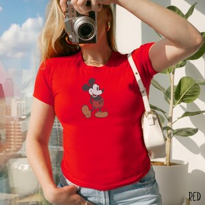 Peut inclure: T-shirt rouge avec un dessin de Mickey Mouse. Le personnage de dessin anim&eacute; est repr&eacute;sent&eacute; dans sa pose classique, avec une t&ecirc;te noire, un visage blanc, un short rouge et des chaussures jaunes. Le t-shirt est &agrave; manches courtes.
