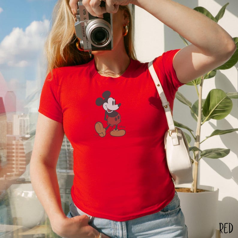 Peut inclure: T-shirt rouge avec un dessin de Mickey Mouse. Le personnage de dessin anim&eacute; est repr&eacute;sent&eacute; dans sa pose classique, avec une t&ecirc;te noire, un visage blanc, un short rouge et des chaussures jaunes. Le t-shirt est &agrave; manches courtes.