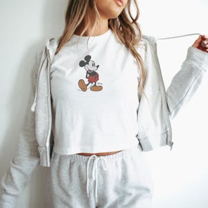 Peut inclure: Haut court blanc avec un motif de Mickey Mouse en noir, rouge et marron. Le design de la marque Disney est centr&eacute; sur le devant du t-shirt. Le haut fait partie d'une tenue d&eacute;contract&eacute;e.