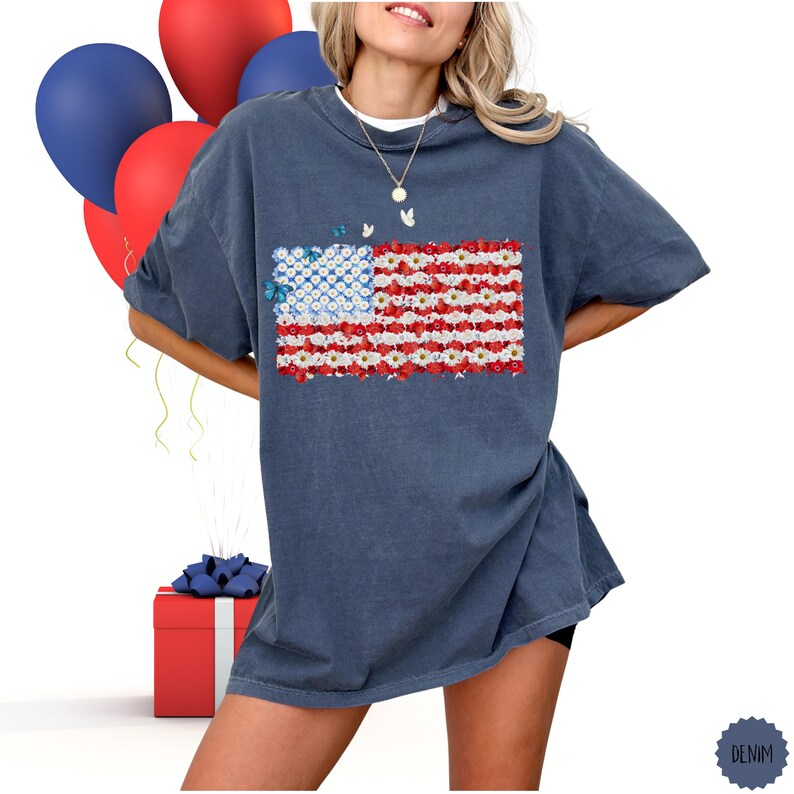May include: A denim blue t-shirt featuring a floral American flag design. The flag's stripes are made of red and white flowers, with a blue flower field in the corner. The shirt is part of a patriotic collection.