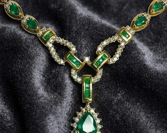 Op de afbeelding: Een gouden ketting met een centrale peervormige smaragdgroene hanger omringd door kleine witte diamanten. De ketting bestaat uit afwisselende marquise-geslepen smaragden en rechthoekige segmenten, geaccentueerd met witte diamanten.