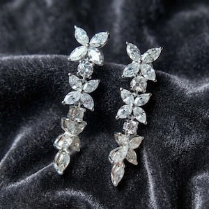 May include: A pair of silver-toned drop earrings featuring a vertical arrangement of marquise and round-cut clear stones. The design consists of multiple flower-like clusters linked together, creating a long, dangling silhouette with high sparkle.