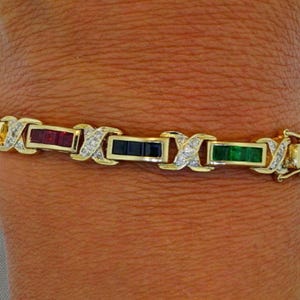 Pode incluir: Uma pulseira de ouro com pedras preciosas retangulares alternadas em vermelho, azul e verde. A pulseira tem detalhes de diamantes e um fecho. As pedras são engastadas em uma corrente de ouro.