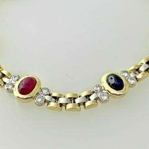 Può includere: Un bracciale bicolore oro e argento con pietre preziose ovali. Presenta un rubino e uno zaffiro, con piccoli diamanti tra le maglie. Le pietre sono incastonate in castoni d'oro.