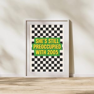 May include: A framed poster with a black and white checkered background. The poster features the text "SHE'S STILL PREOCCUPIED WITH 2005" in yellow and white lettering on a green rectangle.