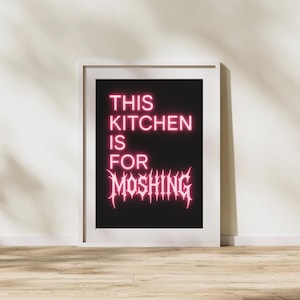 Può includere: Una stampa artistica incorniciata con la scritta "THIS KITCHEN IS FOR MOSHING" in rosa neon su sfondo nero. La stampa è in una cornice bianca ed è esposta su una parete.