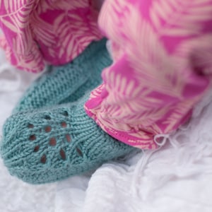 May include: A pair of teal blue knitted baby booties with a lacy pattern. The booties are on a white surface.