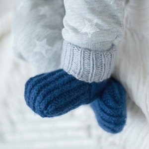 May include: A pair of blue knitted baby booties with a ribbed texture. The booties are on a white background.