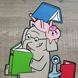 May include: A layered paper cutout illustration featuring a gray elephant wearing glasses and reading a green book. A pink pig balances a blue book on its back while resting on the elephant's head. A blue pigeon sits nearby reading a red book.