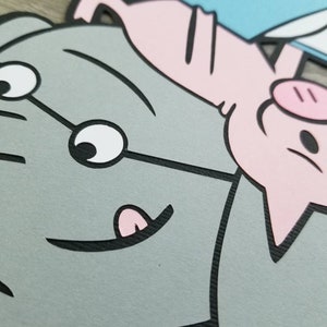 May include: A layered paper cutout featuring a large gray elephant with a smiling expression and a small pink pig positioned above it. The pig is holding a light blue rectangular object. The design uses bold black outlines and flat colors.