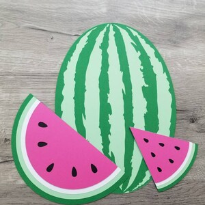 May include: Three paper watermelon shapes, one whole watermelon and two slices. The watermelon is green with black stripes and the slices are pink with black seeds.