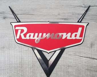 May include: A red and black car-shaped sign with the name "Raymond" in silver lettering.