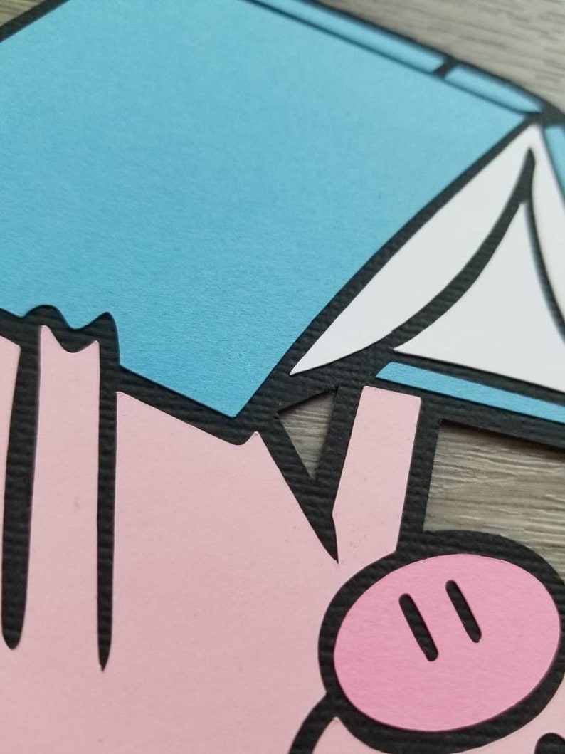May include: A layered paper cutout featuring a stylized pink pig figure with a black outline, positioned beneath a light blue and white geometric shape. The design uses flat, solid colors with a distinct black border separating each paper element.
