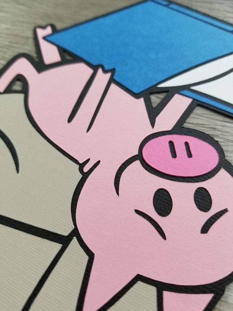 May include: A layered paper cutout featuring a pink pig with a dark pink snout, positioned above a beige shape and holding a blue rectangular object with a white corner. The design uses bold black outlines to define the pig and the geometric shapes.