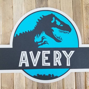 May include: A blue and black dinosaur-themed sign with the name "AVERY" in white outlined letters.