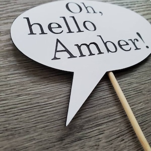 May include: White speech bubble photo booth prop with black text that reads "Oh, hello Amber!"