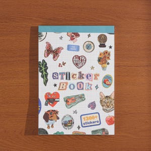 May include: A rectangular sticker book with a white grid background and a teal top binding. The cover features the text "STICKER BOOK" in colorful letters, surrounded by various illustrations including a butterfly, a cat, a dog, and a "1300+ stickers" label.