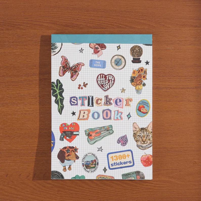 May include: A rectangular sticker book with a white grid background and a teal top binding. The cover features the text "STICKER BOOK" in colorful letters, surrounded by various illustrations including a butterfly, a cat, a dog, and a "1300+ stickers" label.