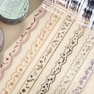May include: Decorative washi tape rolls with floral and lace designs in various colors, including brown, black, and purple. The tape is on a light beige background. The image also shows the text "just a space".