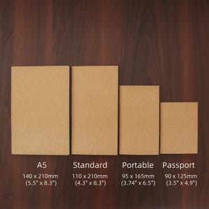 May include: Four kraft paper notebooks of varying sizes are displayed on a wooden surface. The sizes are labeled A5 (5.5" x 8.3"), Standard (4.3" x 8.3"), Portable (3.74" x 6.5"), and Passport (3.5" x 4.9").