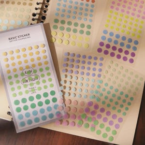 Könnte beinhalten: Eine Auswahl an bunten Punktaufklebern zum Journaling. Die Aufkleber sind auf transparenten Bögen angeordnet, von denen einer den Text "BASIC STICKER ART FOR JOURNALING" und "KNOW YOUR PASSION" trägt.