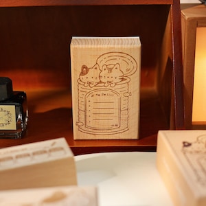 May include: A wooden stamp featuring a whimsical design of two cats in a can, with the words "To Do List" and lined spaces for notes. The stamp is made of light-colored wood and is ideal for stationery and crafting projects.