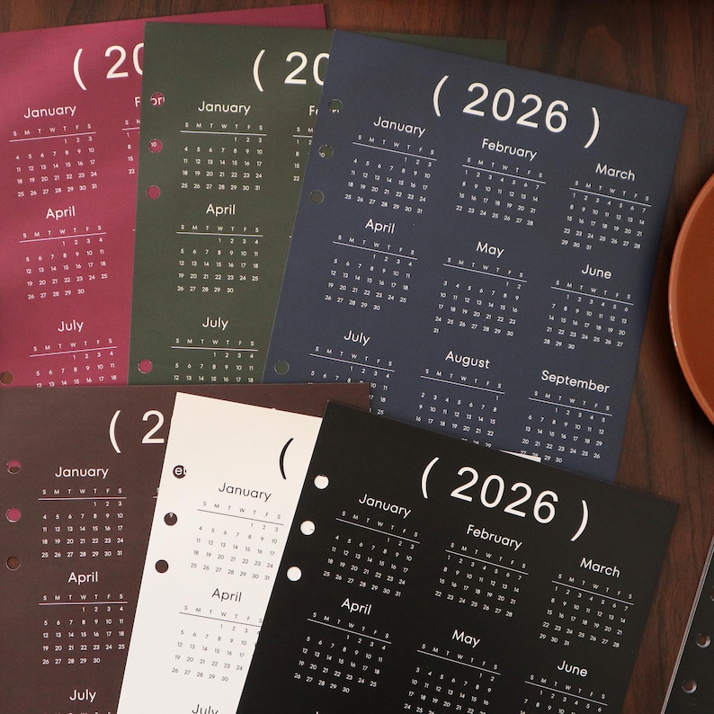 Pu&ograve; includere: Una collezione di pagine di calendario per l'anno 2026 in vari colori, tra cui bordeaux, verde, blu navy, marrone, bianco e nero. Ogni pagina presenta un layout di calendario mensile con il nome del mese e i giorni della settimana.