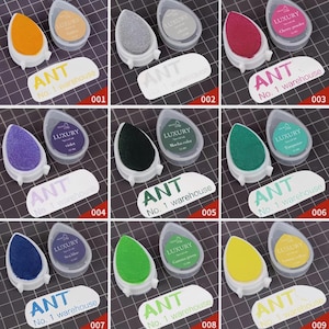 May include: A collection of nine ink pads in various colors, including orange, gray, red, purple, black, green, blue, and yellow. Each pad is paired with a small container labeled "LUXURY" and a label that reads "ANT No. 1 warehouse."