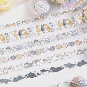 May include: Decorative washi tape rolls featuring various cat designs. The tapes showcase repeating patterns of cartoon cats, paw prints, and cats wearing outfits. The color palette includes shades of gray, orange, and white, with some blue accents.