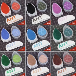 May include: A collection of ink pads in various colors, including orange, black, purple, blue, green, and brown. Each pad is teardrop-shaped and comes with a clear plastic case. The text "LUXURY" and "ANT No. 1 warehouse" are visible.