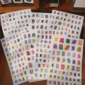 Könnte beinhalten: Mehrere Bögen mit Klebeaufklebern, die eine Vielzahl von Buchstaben und Zahlen in verschiedenen Schriftarten, Farben und Größen zeigen. Jedes Zeichen ist in einem eigenen, unregelmäßig geformten Rahmen dargestellt, der wie ausgeschnittene Zeitungsartikel wirkt.
