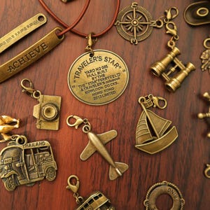 Peut inclure: Une collection de breloques et de pendentifs de voyage en laiton antique. Comprend une boussole, des jumelles, un voilier, un avion, un appareil photo et un pendentif avec le texte "Traveler's Star". Le mot "ACHIEVE" est également visible.