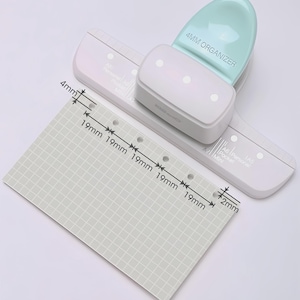 May include: A white and mint green 4mm organizer hole punch with a matching ruler guide. A gray grid paper shows measurements of 19mm and 4mm. The punch is labeled "4MM ORGANIZER".